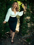Micheline Pitt stepping through a green door in a garden setting while modeling the Vamp Pencil Skirt in Dark Green from gothic retro clothing brand La Femme en Noir.