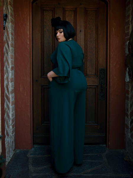 A back shot of Megan standing in front of a door while modeling the Black Widow palazzo pants in hunter green.