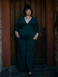 Megan stands in front of a door while modeling the Black Widow palazzo pants in hunter green.