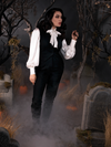 Standing in a foggy cemetery scene while holding on a branch of a dead tree, Micheline Pitt models the Sleepy Hollow Ichabod Pants in Black.