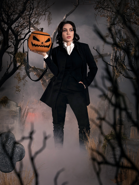 Micheline Pitt dressed as Ichabod Crane, holds the Sleepy Hollow Pumpkin Bag up on the palm of her hand.