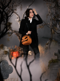 Micheline Pitt walking through a foggy cemetery holding a pumpkin bag on her shoulder to show off the Sleepy Hollow Ichabod Pants in Black.