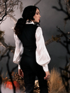 Micheline Pitt dressed as Ichabod Crane, facing away from the camera with her head slightly turned back towards it, wearing the Sleepy Hollow Ichabod Vest in Black from gothic clothing company La Femme en Noir.