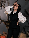 Micheline Pitt standing in front of a foggy forest setting wearing a gothic style outfit from La Femme en Noir.