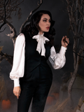 With her hand resting on a branch from a dead tree, Micheline Pitt looks into the distance while posing in her Victorian Blouse in Ivory from La Femme en Noir.