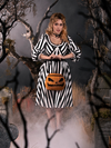 Linda holding a pumpkin bag while standing in a foggy cemetery while wearing a black and white striped gothic dress.