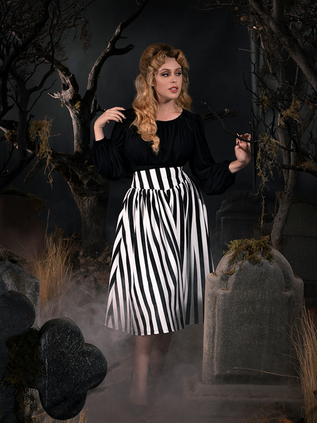 Linda resting her hand on the branch of a dead tree next to her models the  Sleepy Hollow The Katrina Skirt in Black and White from gothic retro clothing brand La Femme en Noir. 
