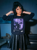 Raven haired model standing in a spookily lit room wearing the BEETLEJUICE™ Ghost Sweatshirt with matching vegan leather skirt.