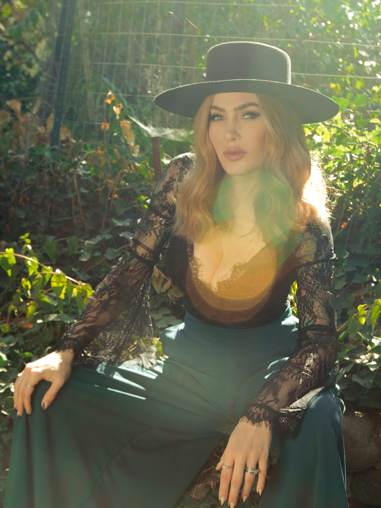 Sitting in her sunny garden, Micheline Pitt models the La Sorcière Top in Black from La Femme en Noir.