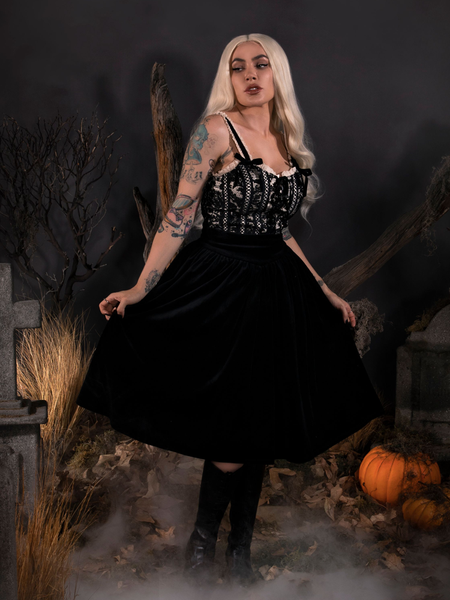 Looking away while holding her skirt with both hands, Micheline Pitt models the Sleepy Hollow Gothic Tales Velour Skirt in Black from La Femme En Noir.