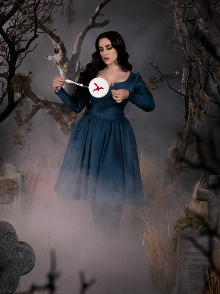 The Sleepy Hollow The Lady Crane Dress in Vintage Blue modeled by Rachel while standing next to tombstones in a foggy graveyard.