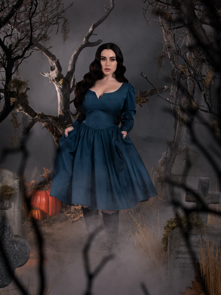 Rachel holding out the sides of the skirt section of her Sleepy Hollow The Lady Crane Dress in Vintage Blue to while posing in a fog-laden, cemetery scene. 