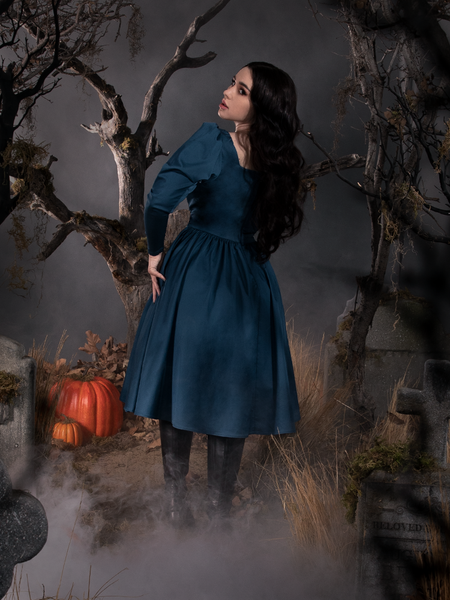Rachel, with her body facing away from the camera but her head turned back towards it, shows off the Sleepy Hollow The Lady Crane Dress in Vintage Blue from La Femme en Noir.