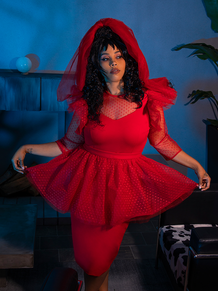 Female model holds out the sides of the skirt of the BEETLEJUICE™ Lydia Dress while standing in a quirky and spooky living room.