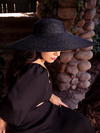 Ashley slightly looking downward while wearing the Lydia Sun Hat with matching black goth dress from La Femme en Noir.