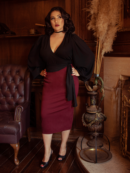 Erika standing next to a fireplace and leather chair while modeling the Vamp pencil skirt in oxblood.