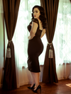 A back shot of Rachel standing in front of a window modeling the Vamp pencil skirt in black by La Femme En Noir.