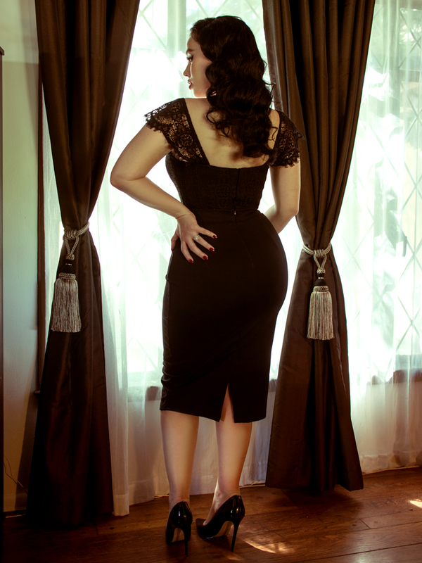 A back shot of Rachel standing in front of a window modeling the Vamp pencil skirt in black by La Femme En Noir.