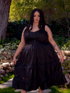 Amidst the blooming flowers of a radiant garden, a brunette muse captures attention with her grace, adorned in the captivating Pickety Witch Dress in Black, a gothic masterpiece by La Femme en Noir.