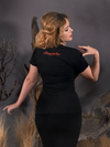 Linda is turned away from the camera and showing off the back of the Sleepy Hollow™ Protection Spell Tee from La Femme En Noir.