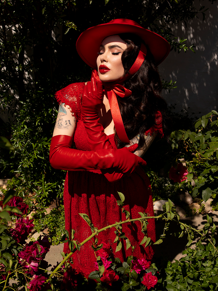 Micheline Pitt posing in her garden while in an all crimson gothic retro clothing outfit including the Southern Gothic Bustier Top in Crimson.