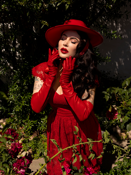 Micheline Pitt with her hands gently touching her chin wears the Southern Gothic Bustier Top in Crimson.