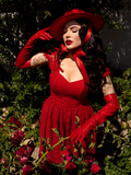 Micheline Pitt standing in a rose garden while wearing an all crimson gothic style outfit.