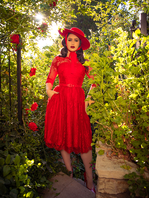 Full length shot of Ashley standing in a red rose garden in the Mourning Dress in Crimson Lace From goth dress maker La Femme en Noir.