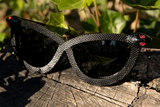 Close up shot of the Serpent Sunglasses in Black from La Femme en Noir sitting on top of a old, wooden log.