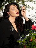 Micheline Pitt closing her eyes while posing in an open black flowy top accented by the Black Widow Rhinestone Spider Brooch.