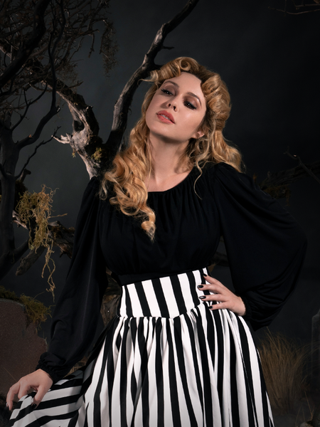 Linda standing in a goth graveyard in a gothic top wearing a black and white stripe skirt.