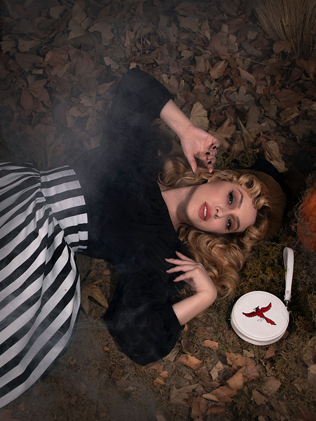 Linda laying on the leaf covered ground wearing the Salem Top in Black.