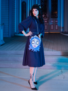 Full length shot of female model wearing the Salem Dress in Navy with an Emily Corpse Bride bag hanging off of her shoulder.