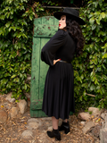 Micheline Pitt photographed in front of a green door in a garden wearing a gothic dress.