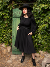 With her hands tucked into her pockets, Micheline Pitt models the Salem Dress in Black. 