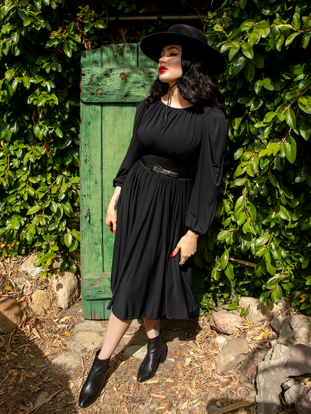 Full length shot of Micheline Pitt wearing a black gothic style dress with matching sunhat and ankle boots.