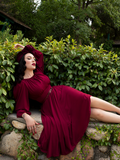 Micheline Pitt laying down on a stone bench while showing off the Salem Dress in Oxblood.