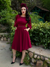 With her hands in her pockets, Micheline Pitt shows off a ravishing blood red gothic dress from La Femme en Noir.
