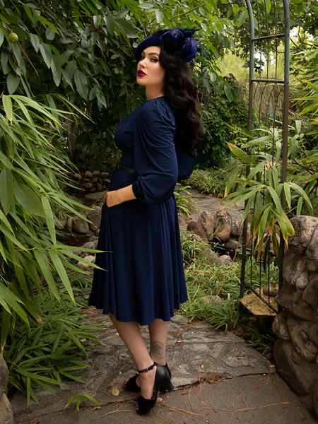 Turned to the side, Micheline Pitt shows off the Salem Dress in Navy from gothic clothing house La Femme en Noir.