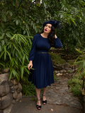 Micheline Pitt photographed in a lush green garden while wearing the Salem Dress in Navy. 