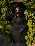 Micheline Pitt letting small slivers of sunlight wash over her face, wears the Salem Top in Black from La Femme en Noir.