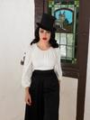 Micheline Pitt staring directly into the camera mid-strut while wearing the Salem Top in Ivory.