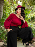 Micheline Pitt posing with her leg up on a rocky ledge while wearing a gothic style top called the Salem Top in Oxblood.