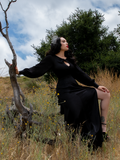 Sat on a downed tree we get a profile shot of Micheline Pitt while she wears the Opera Satin Gown in Black from La Femme en Noir.