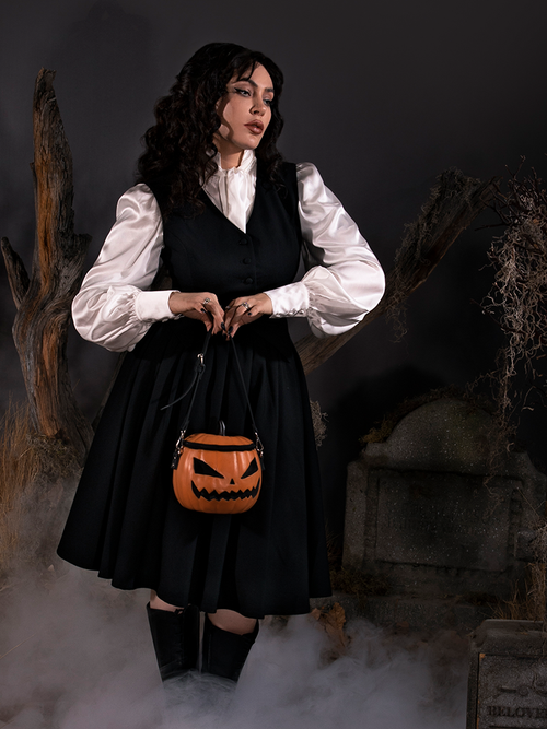 Standing in a foggy cemetery while carrying a pumpkin bag, Micheline models the Sleepy Hollow™ Ichabod Swing Skirt from La Femme En Noir.