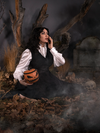 Sitting in a foggy cemetery while holing a pumpkin bag, Micheline models the Sleepy Hollow™ Ichabod Swing Skirt from La Femme En Noir.