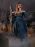 Standing in a foggy cemetery with her hands on her shoulders, Linda models the Sleepy Hollow The Lady Crane Dress in Vintage Blue by La Femme En Noir.
