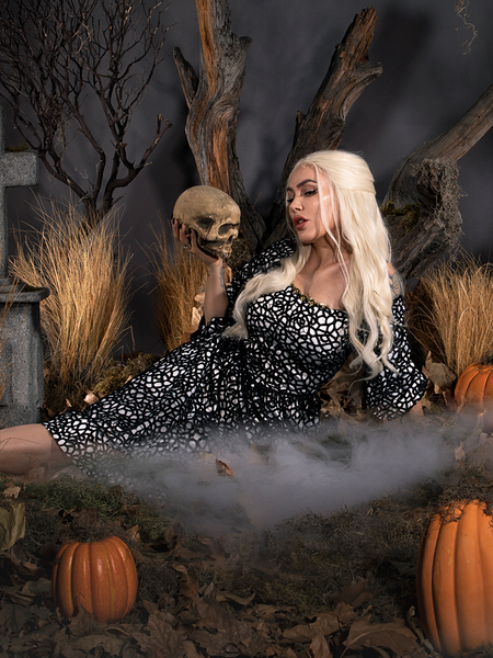 Sitting in a foggy cemetery holding a skull in her hand, Micheline models the Sleepy Hollow™ Lady Van Tassel Guipire Lace Dress from La Femme En Noir.