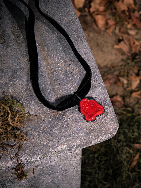 Perched on a tombstone, a detailed closeup of the Sleepy Hollow™ Van Garrett Wax Seal Necklace by La Femme En Noir.