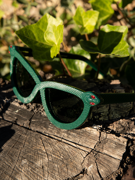 Image of the gothic style Serpent Sunglasses in Emerald Green sitting on top of a rotted out piece of wood.
